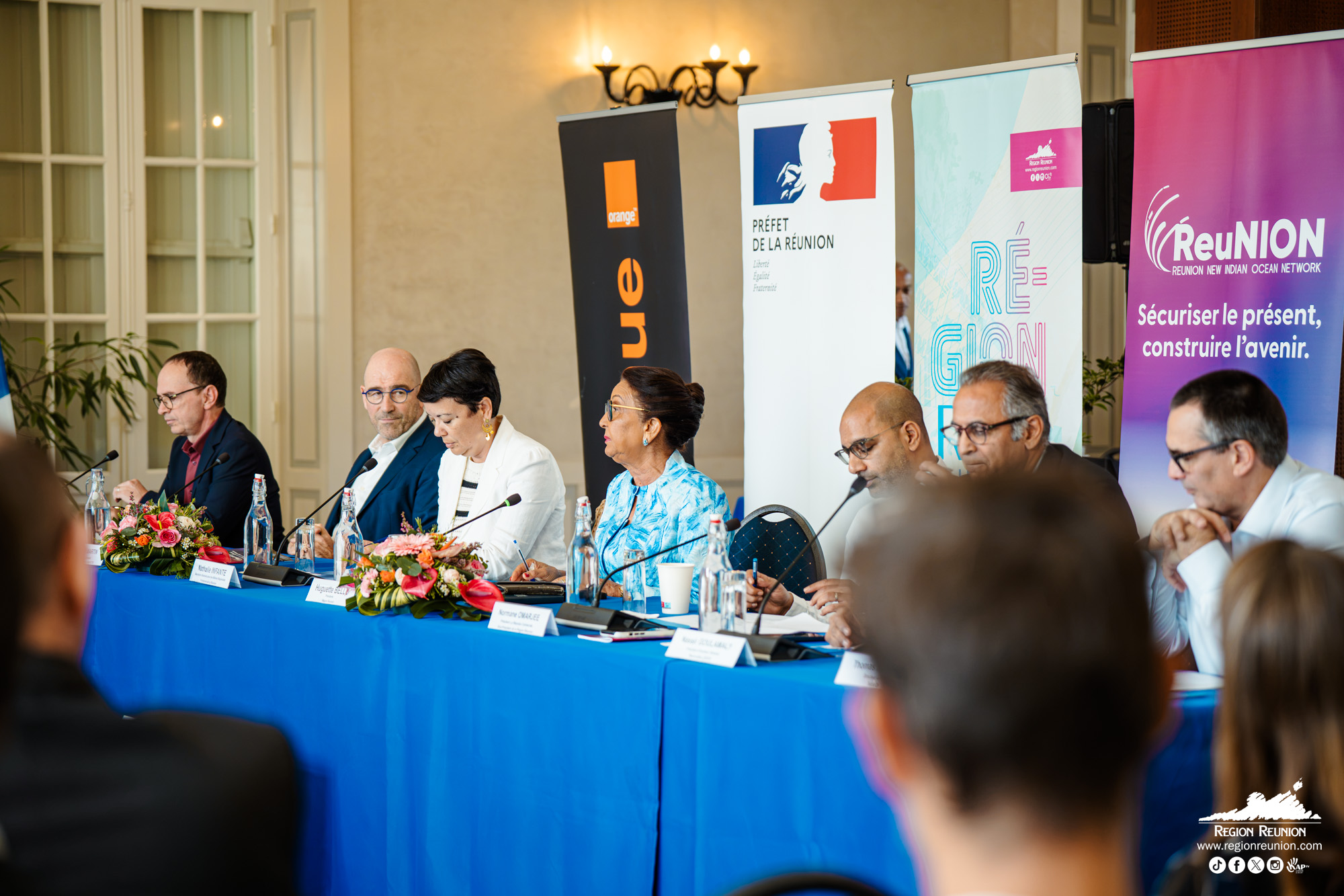 Participants assis autour d'une table lors d'une conférence officielle à La Réunion avec des panneaux institutionnels.