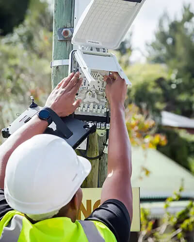 Technicien en équipement de sécurité installant un boîtier de raccordement fibre optique sur un poteau